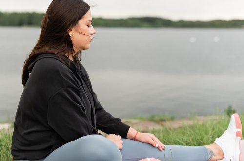 Woman meditating outdoors by a tranquil lakeside, fostering health and wellness.