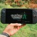 A hand holding a handheld gaming console displaying the Pokémon Legends game screen outdoors.