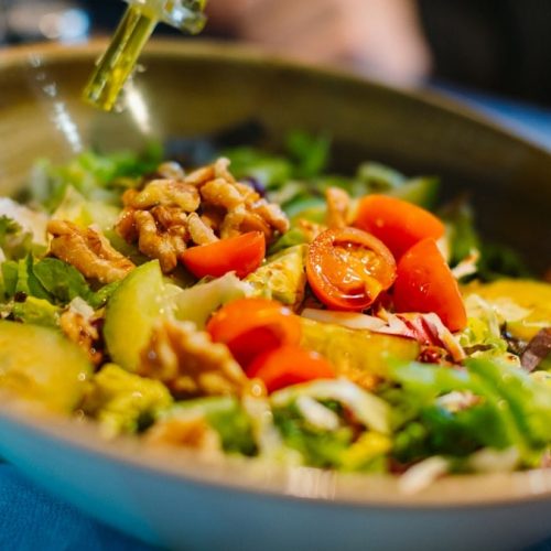 a salad in a bowl with dressing being drizzled over it