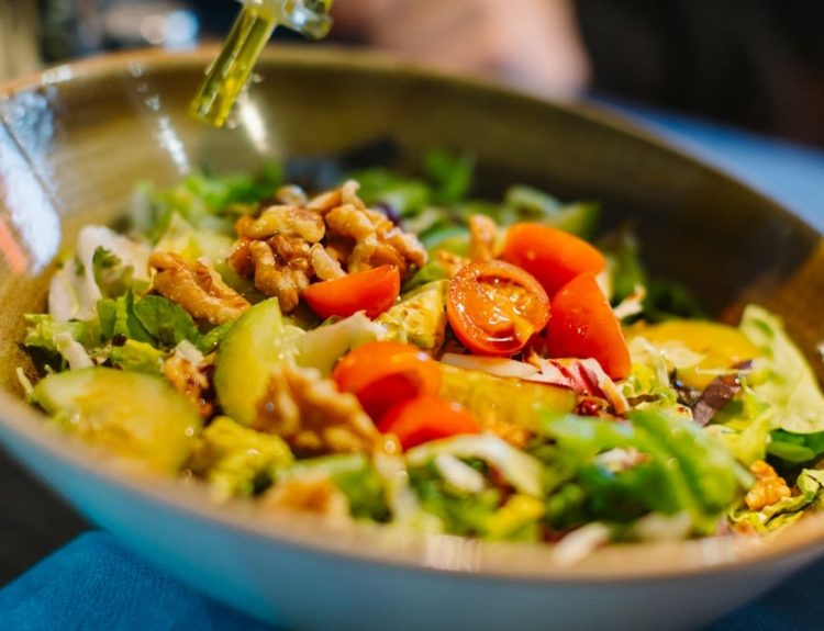 a salad in a bowl with dressing being drizzled over it