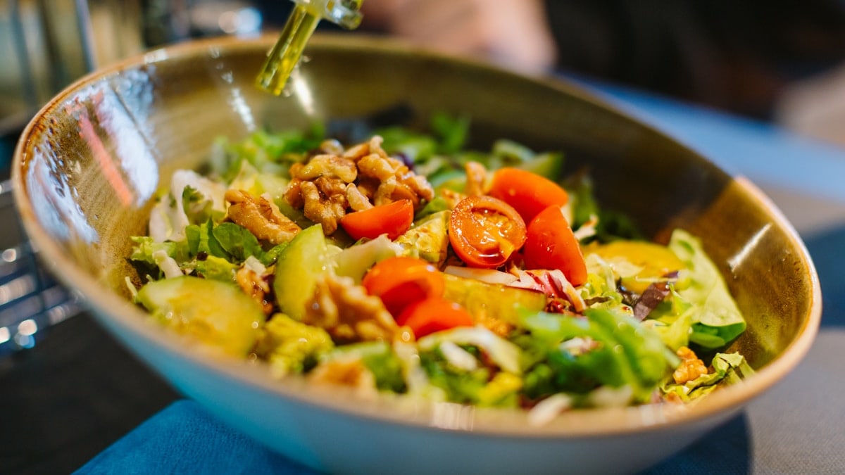 a salad in a bowl with dressing being drizzled over it