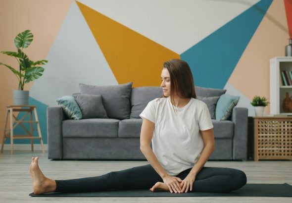 Attractive girl in leggings and T-shirt is doing stretching exercises on yoga mat relaxing on floor at home busy with practise. Youth, lifestyle and health concept.