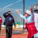 A senior woman joyfully crosses the finish line in a fun run event outdoors.