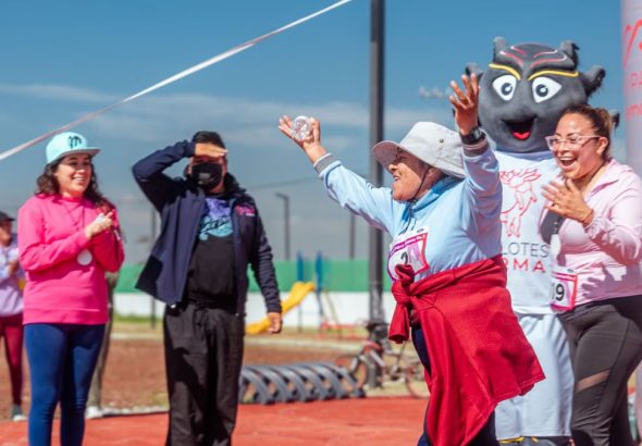 A senior woman joyfully crosses the finish line in a fun run event outdoors.