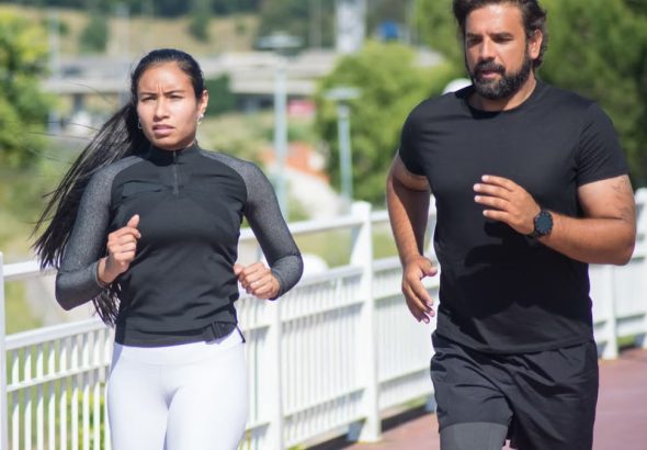 Active couple jogging outdoors on a sunny day, promoting fitness and healthy lifestyle.